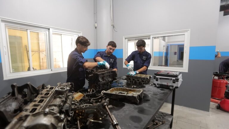 Three students performing hands-on engine training at a workbench.