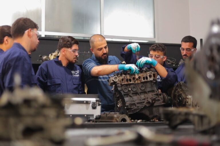 Male instructor and students working on car engine in mechanics workshop classroom