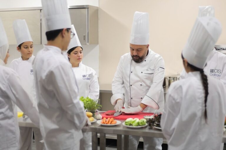 Chef instructor in white uniform working with female students in professional kitchen during cooking class
