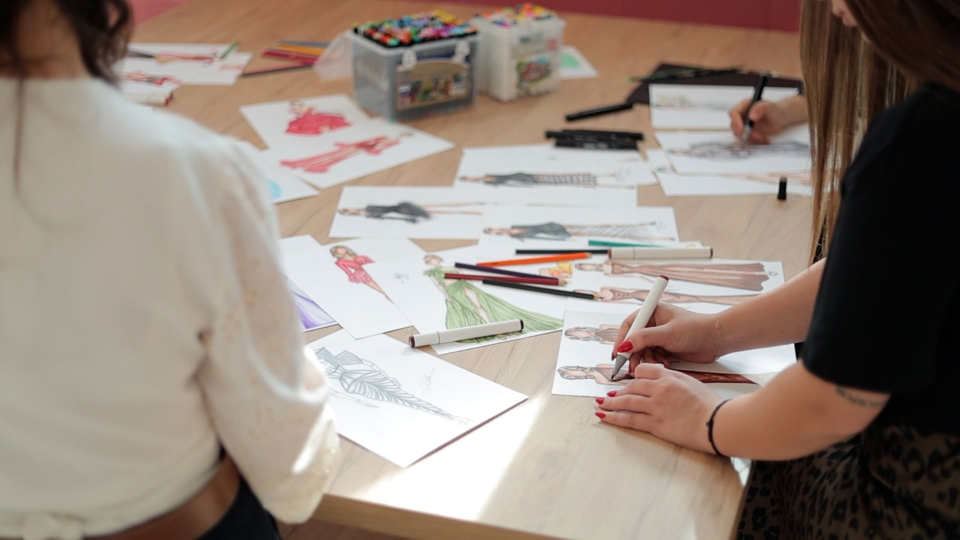 Overhead view of hands working on fashion design sketches.