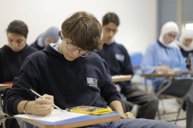 Female student in CIS uniform working on written assignment at classroom desk with glasses